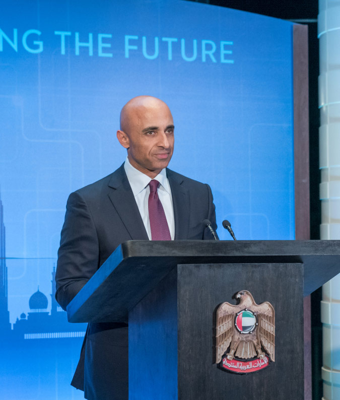 The United Arab Emirates Ambassador to the US, Yousef Al Otaiba, speaks at an event. The UAE's official seal is featured on the podium.